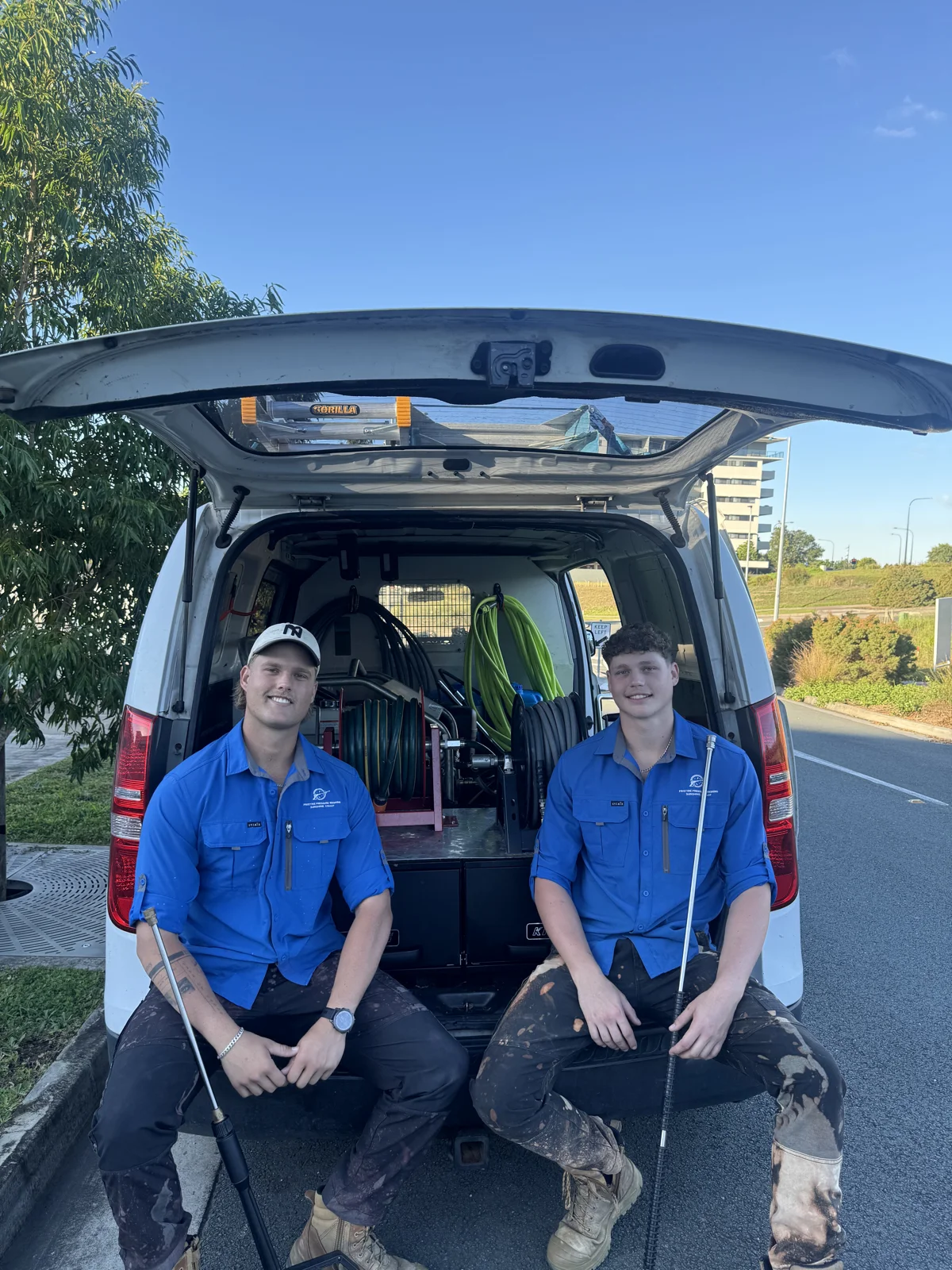 Nick and Matt from Pristine Pressure Washing sitting in the back of their work van with the equipment behind them