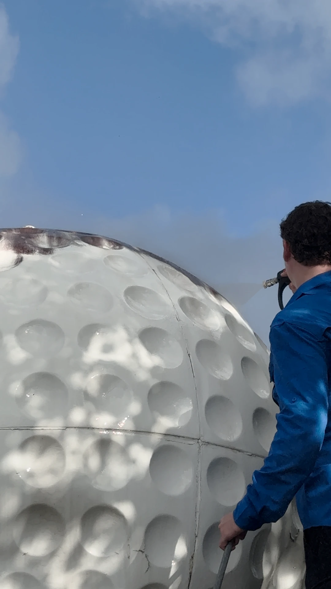 Pristine team member pressure washing a large commercial structure under a blue sky